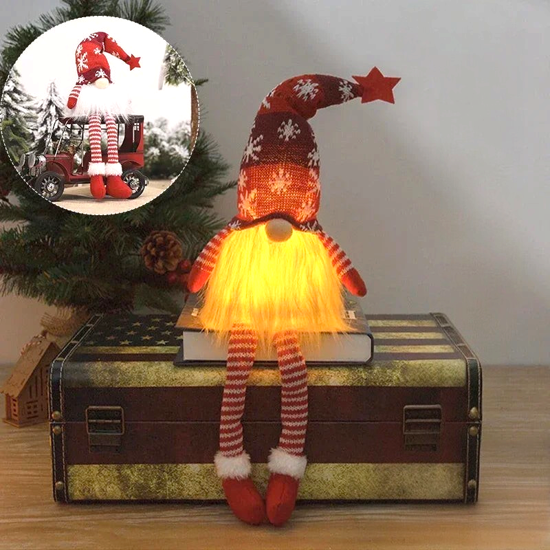 By Levin red plush Christmas gnome with LED light, knitted snowflake hat, and dangling striped legs on a trunk.