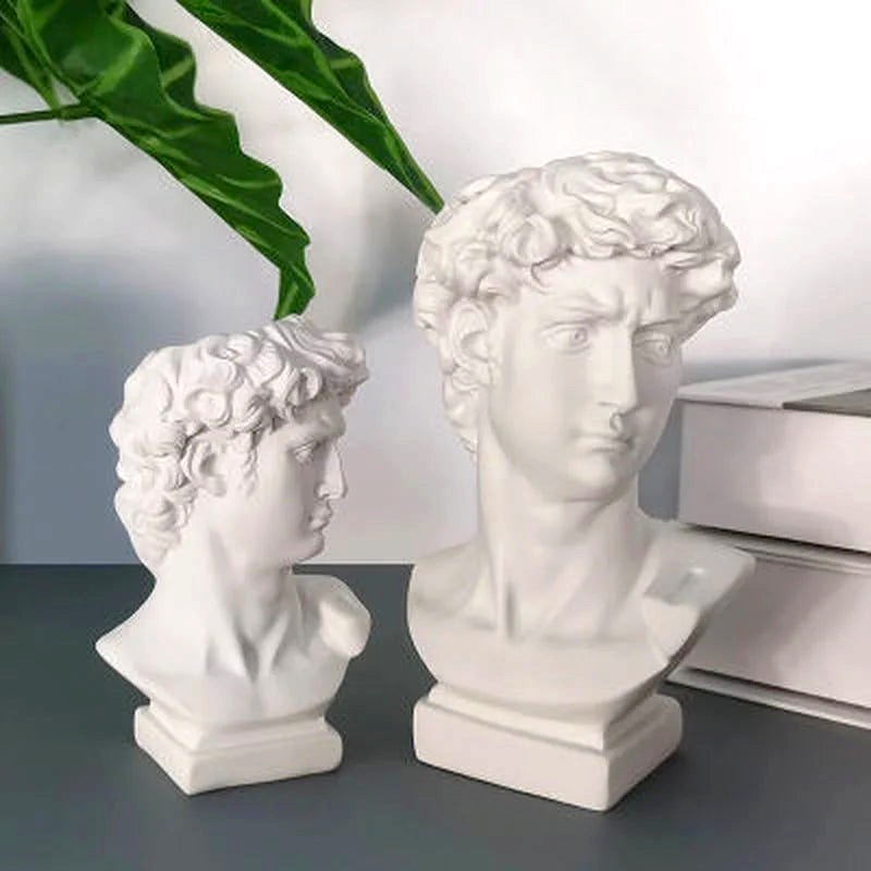 By Levin white resin David bust statues used as decorative vases and brush holders on a desk with green leaves.