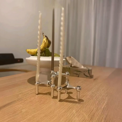 By Levin zilveren moleculaire kandelaar met dinerkaarsen op een houten eettafel in een modern Scandinavisch interieur