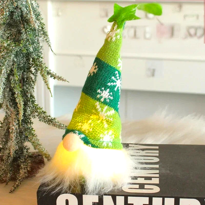 By Levin green knitted Christmas gnome with LED light, snowflake hat, and star topper, sitting on a book.